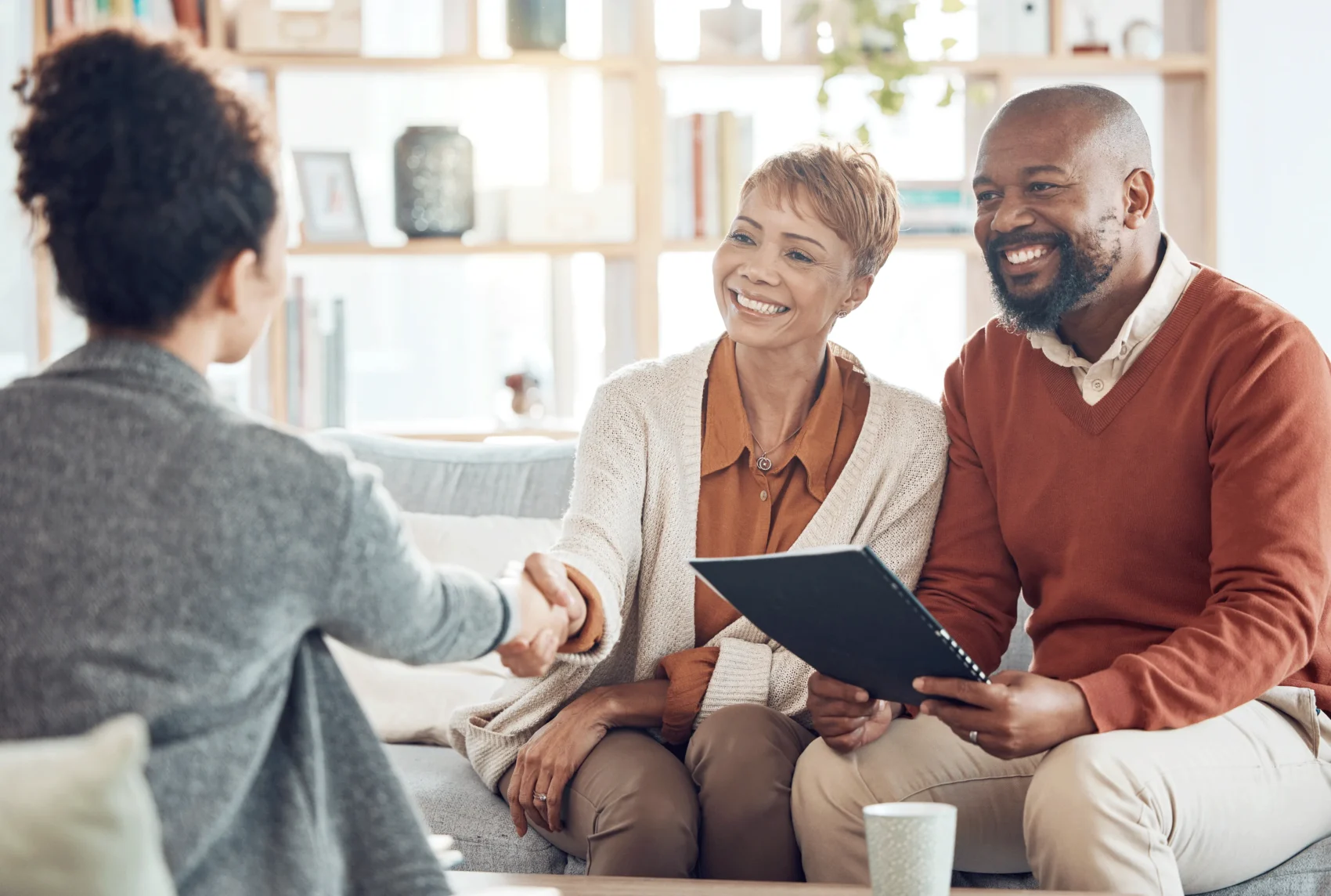 A couple has a business meeting with an insurance professional or financial advisor, while shaking her hand.