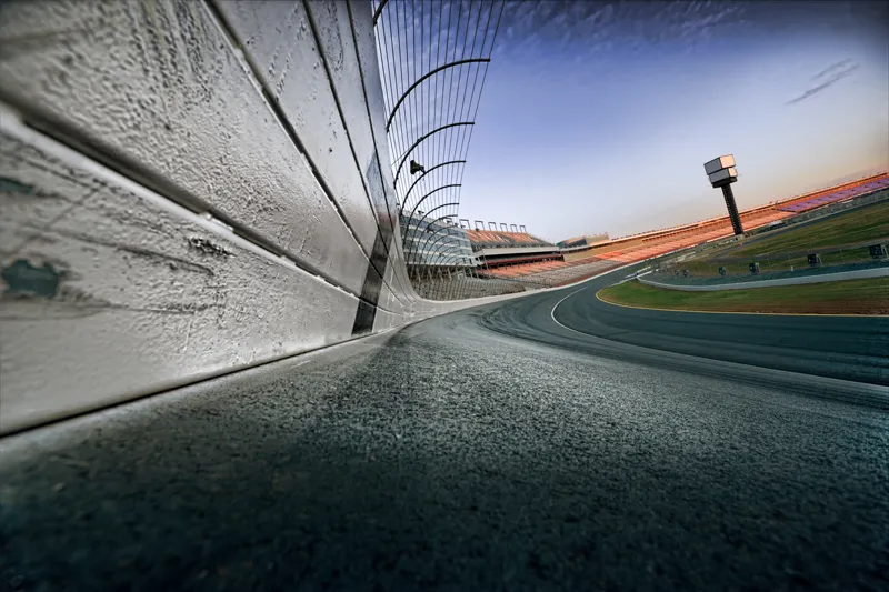 Low-angle view of a curved racetrack with safety fencing and grandstands at sunset, capturing the speed and precision of a track day event—emphasizing the value of Track Day Insurance.