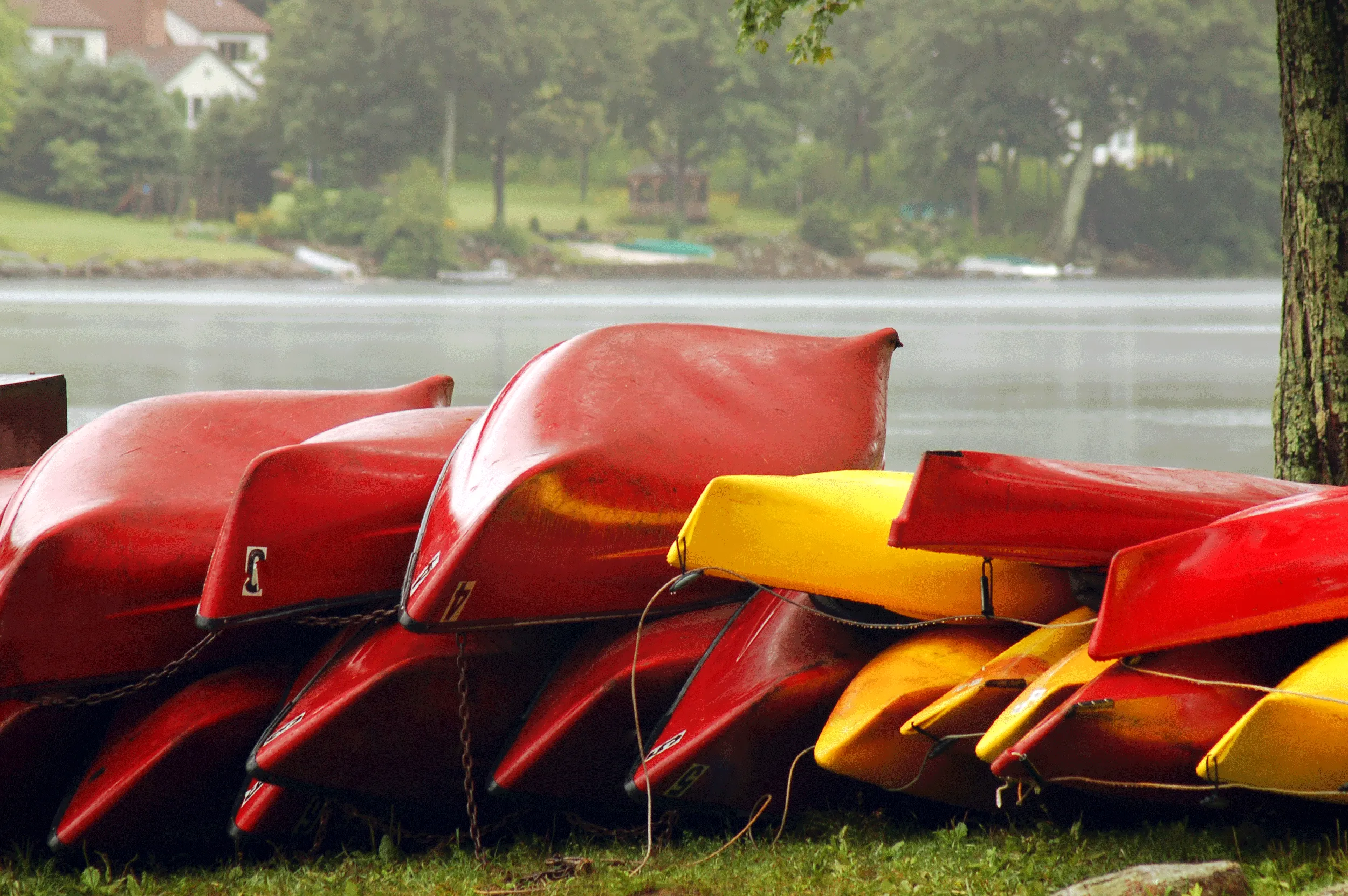 Stacked canoes at a lakeside camp waterfront, representing boating activities and exposures covered by camp insurance.