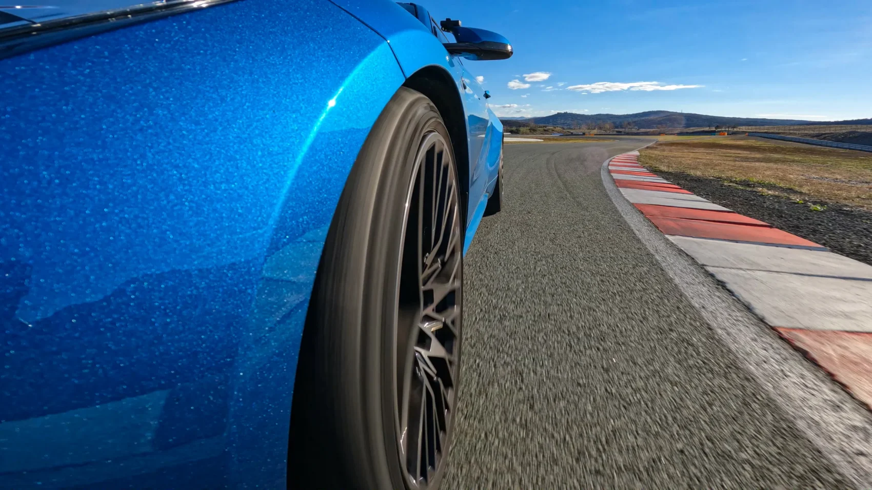 Low-angle view of a blue sports car on a road course during a track day event, emphasizing the importance of track day insurance protection