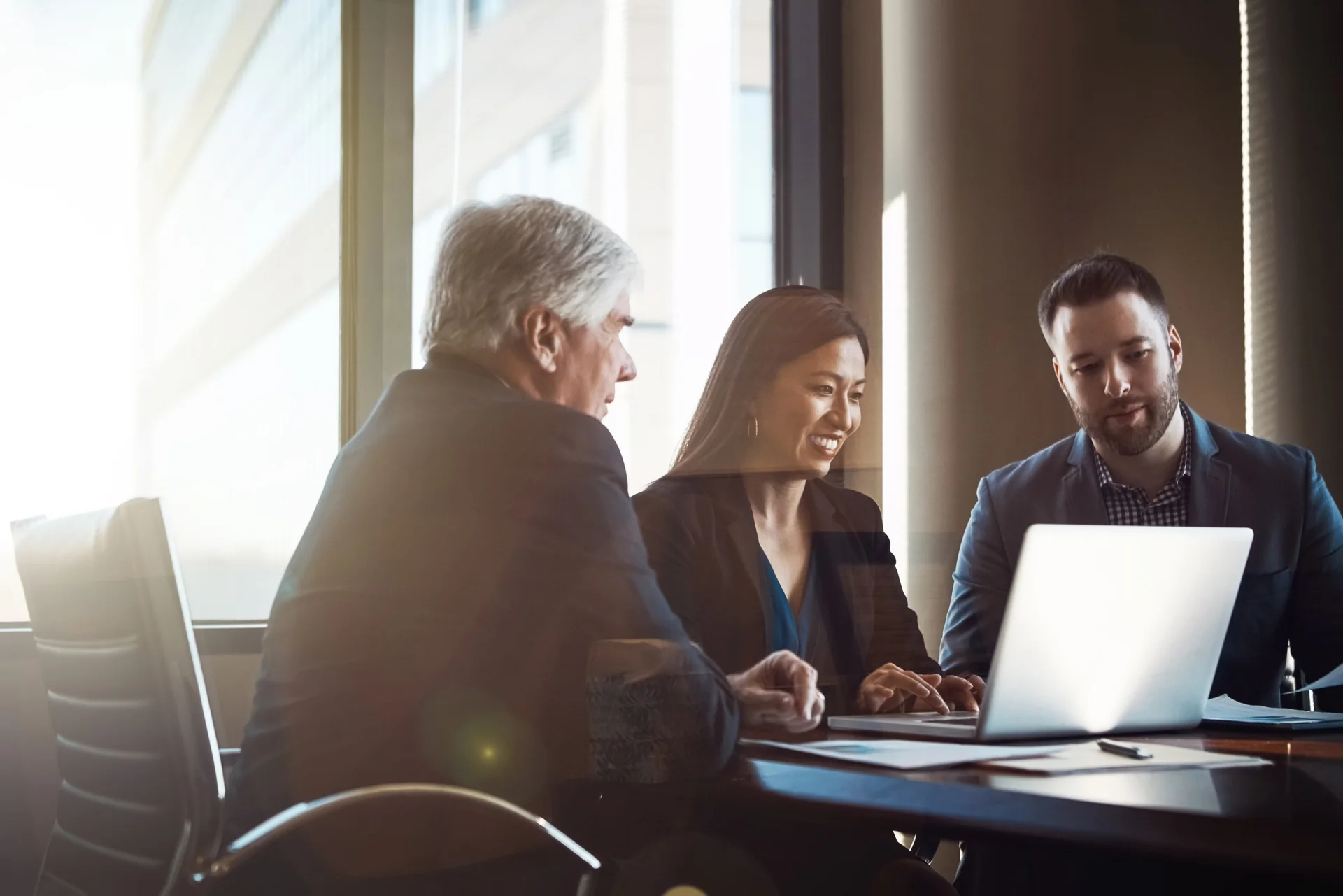 Three people gathered around a laptop at a meeting table